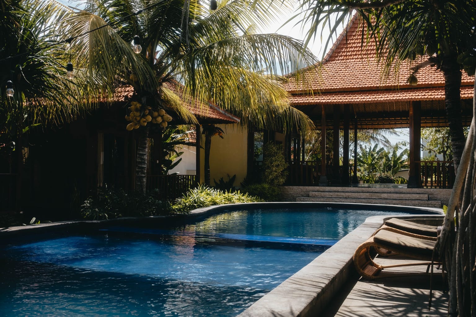 A resort pool surrounded by palm trees and a traditional pavilion.