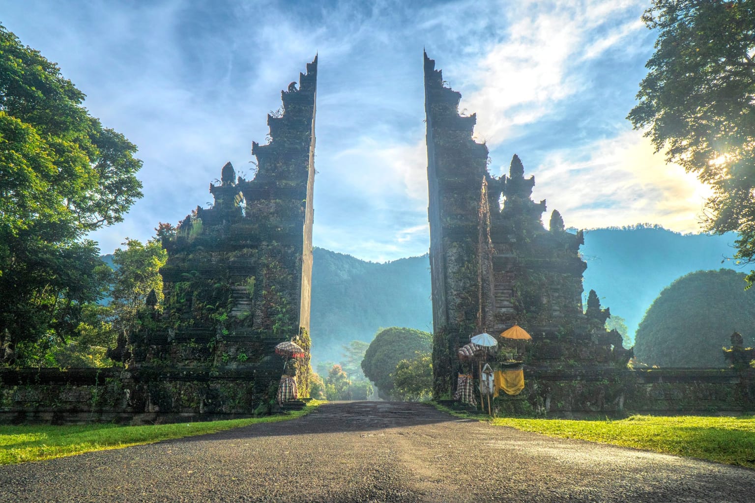 A tall Balinese temple gate framing a road and green mountains at sunrise.